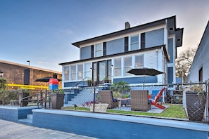 Een modern gebouw met twee verdiepingen, met een blauwe gevel en witte details. Er is een omheind patio met tuinmeubilair en potplanten.