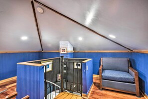 Ein Zimmer mit schrägen Wänden, Holzboden, blauer Wand und einem blauen, gepolsterten Sessel sowie einem kleinen Tisch.