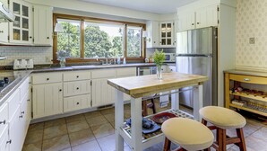 Eine Küche mit weißen Schränken, einer Holz Arbeitsplatte, einem Edelstahl-Kühlschrank und einem Fenster mit Blick auf Bäume.