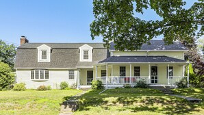 Ein zweistöckiges Haus mit Veranda, Schornstein und gepflegtem Rasen.