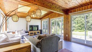 Ein modernes Wohnzimmer mit Holzbalkendecke, großen Fenstern und einem Flachbildfernseher.