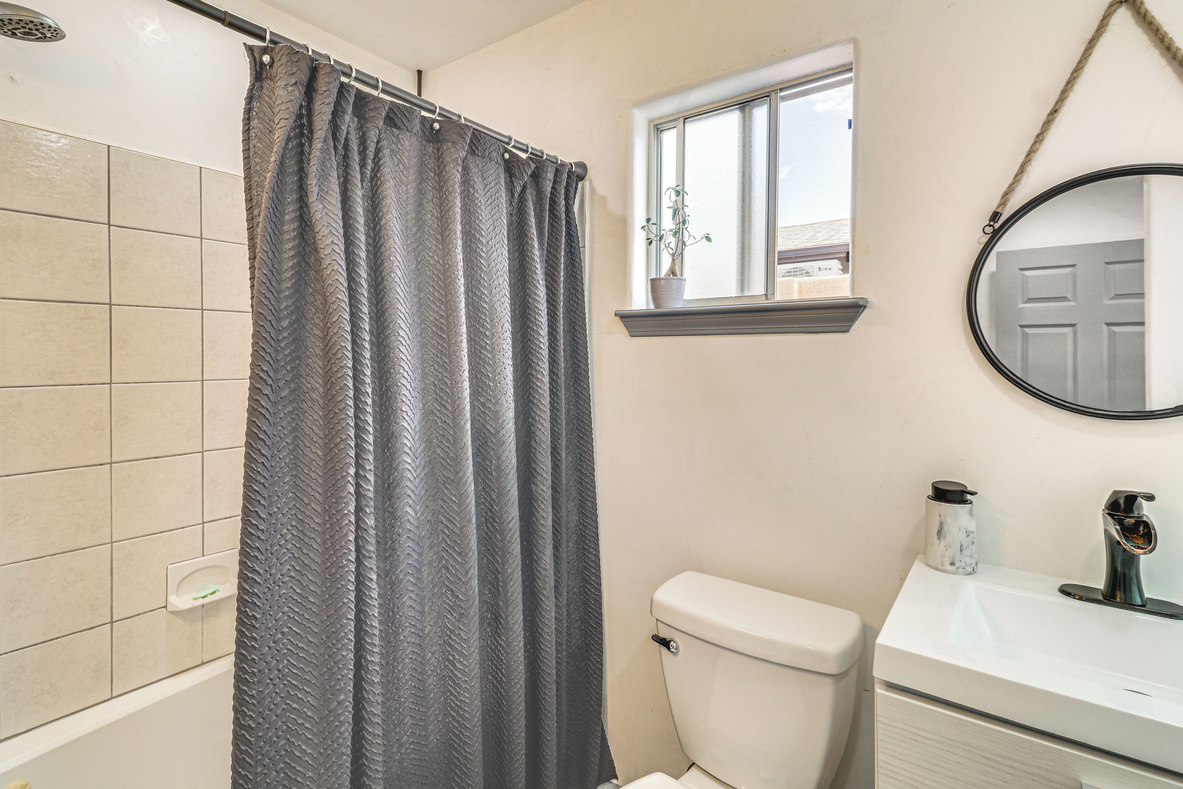 Un bagno con tenda doccia, un water, un lavandino con uno specchio e una finestra con una pianta.