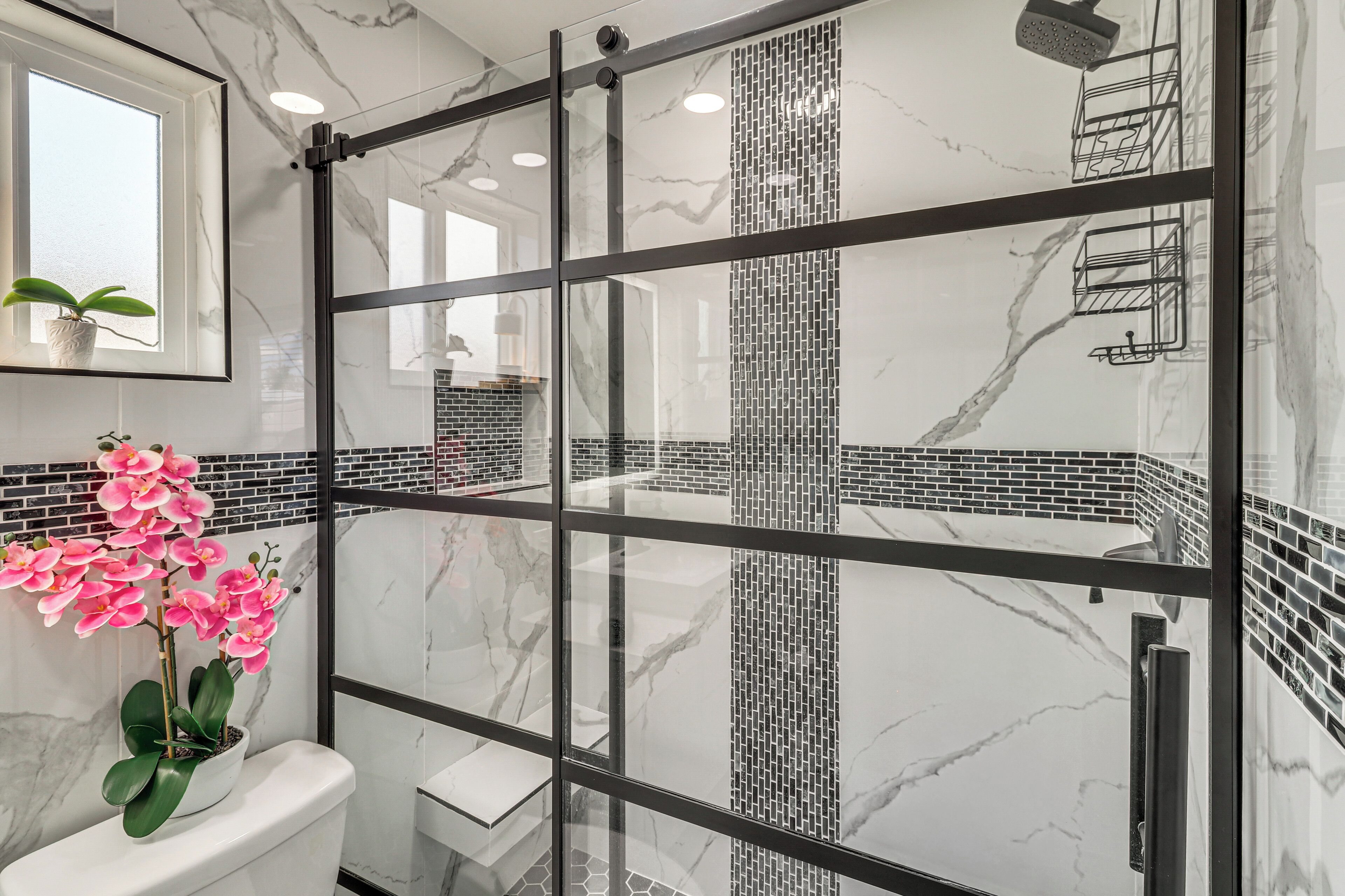 Une salle de bain avec une paroi en verre, des toilettes, un lavabo et une orchidée en pot.