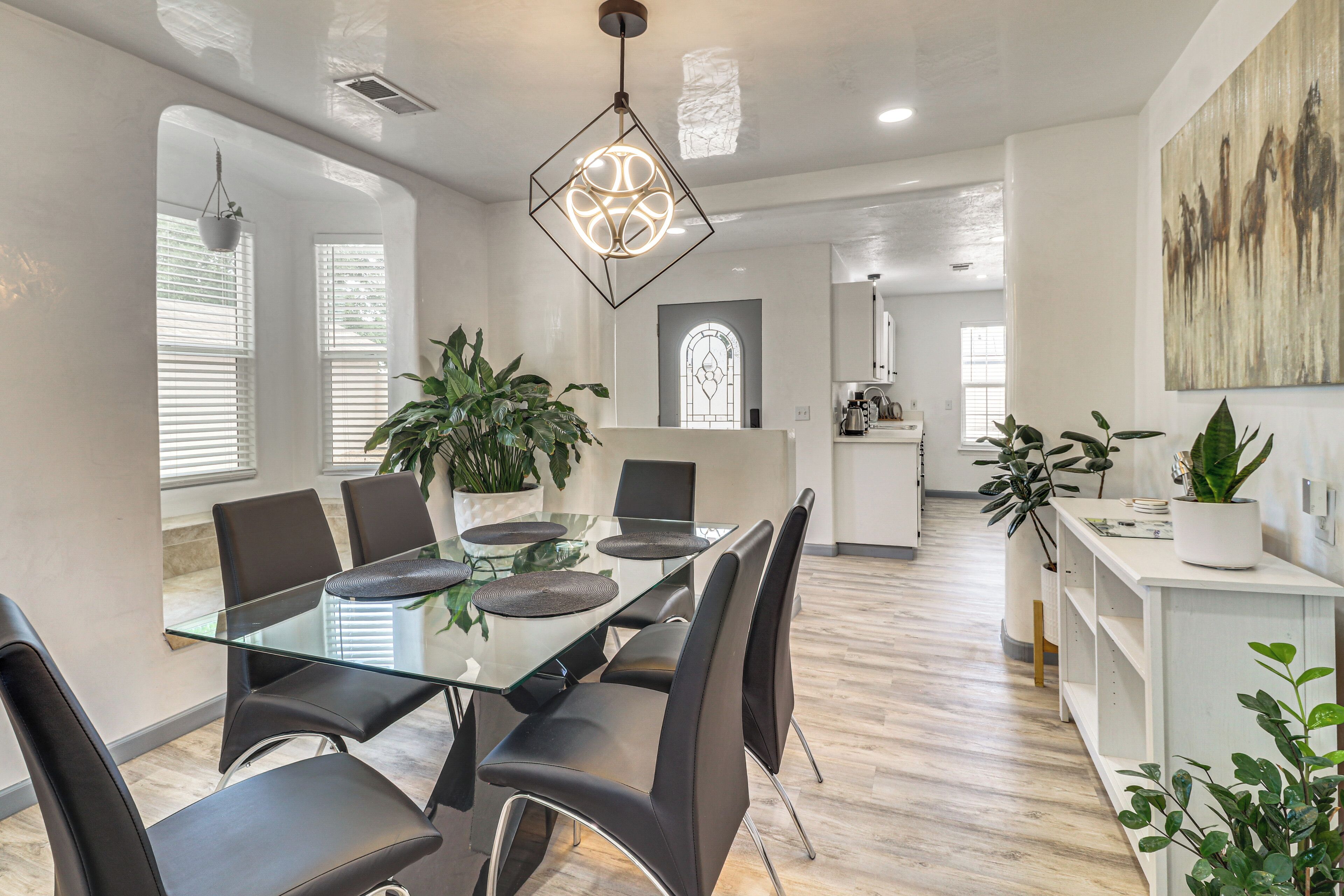 A modern dining area with a glass table, black chairs, and a geometric pendant light.