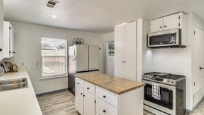 A compact kitchen with white cabinets, a built-in microwave, a gas stove, and a window with blinds. - Room for 6 Cars on Balloon Fiesta Weekend (Albuquerque)