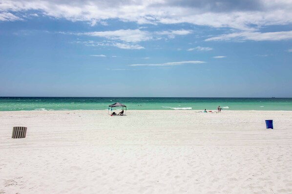 Une plage avec un ciel dégagé, une mer calme et quelques personnes au loin.