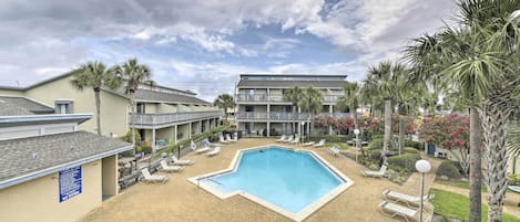 Ein Swimmingpool, umgeben von Liegestühlen und Palmen, mit einem Gebäude im Hintergrund.