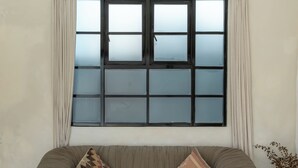 Ein modernes Wohnzimmer mit großem Fenster, einer Couch mit Kissen, einem Couchtisch mit Dekoration und einer Topfpflanze.