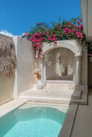 A pool area with a clear blue pool, a white wall, and a thatched roof structure. - Casa Solea (Badung)