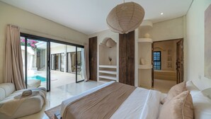 Ein Schlafzimmer mit einem großen Bett, einer Couch, Blick auf einen Pool und einer Schiebetür zu einem Außenbereich.