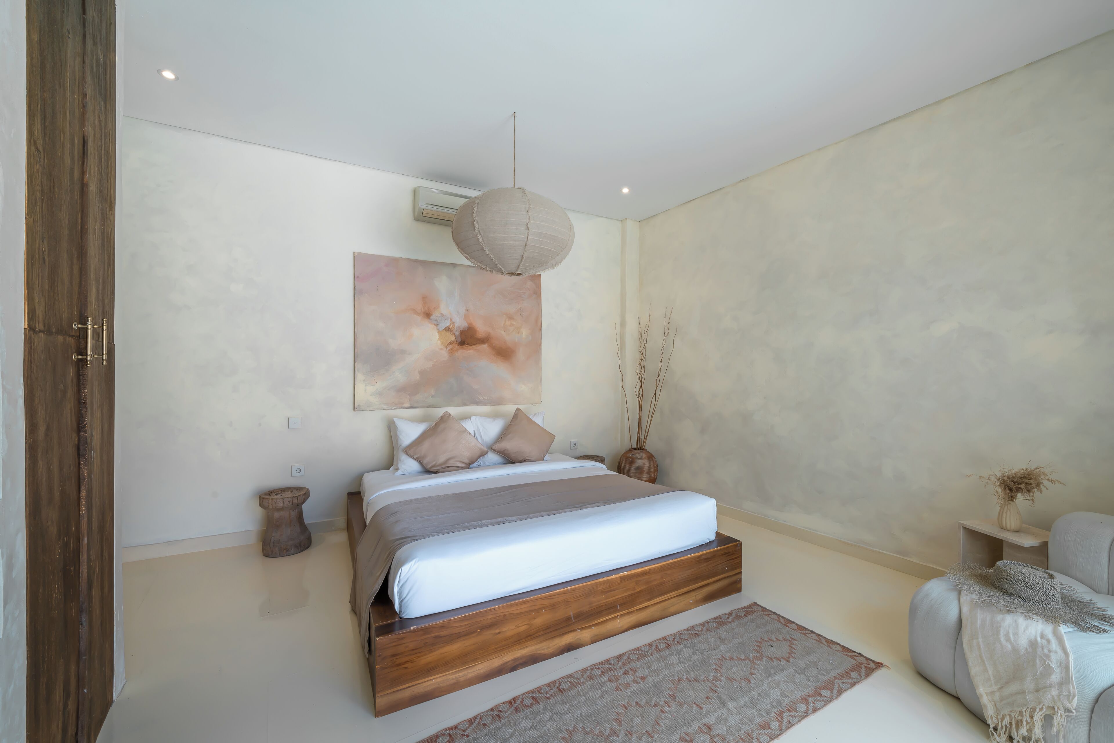 A modern bedroom with a wooden bed, a large abstract painting, and a hanging light fixture.