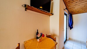 A room with a wooden ceiling, a television mounted on the wall, a table with a yellow tablecloth, a bottle of wine, and a vase with flowers. - Amazing apartment in Viganj with WiFi (Viganj)