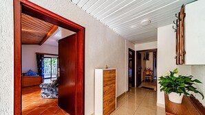 A hallway with a wooden door leading to a room with a bed and a view of greenery outside. There is a white cabinet with drawers and a potted plant on a wooden table. - Amazing apartment in Viganj with WiFi (Viganj)