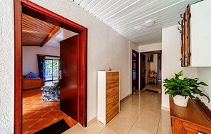A hallway with a wooden door leading to a room with a bed and a view of greenery outside. There is a white cabinet with drawers and a potted plant on a wooden table. - Amazing apartment in Viganj with WiFi (Viganj)