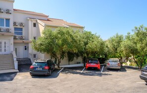 Ein Parkplatz mit drei Autos, einem Gebäude mit Klimaanlagen und Bäumen.