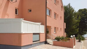 A multi-story building with a flat roof, white shutters on the ground floor, and a small outdoor area with steps leading to a door. - Gorgeous apartment in Orebic with WiFi (Orebic)