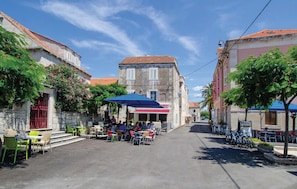 A street with outdoor seating, a building with a red-tiled roof, and a clear blue sky.