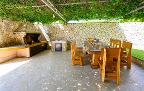 An outdoor kitchen area with a stone wall, a built-in grill, and wooden furniture. - Beautiful apartment in Sreser with WiFi (Sreser)