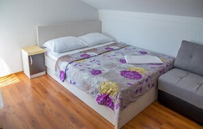 A bed with a floral bedspread, a bedside table, and a grey sofa in a room with wooden flooring. - Beautiful apartment in Sreser with WiFi (Sreser)
