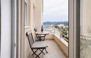 Un balcon avec une table et deux chaises, offrant une vue sur la côte et les montagnes au loin.