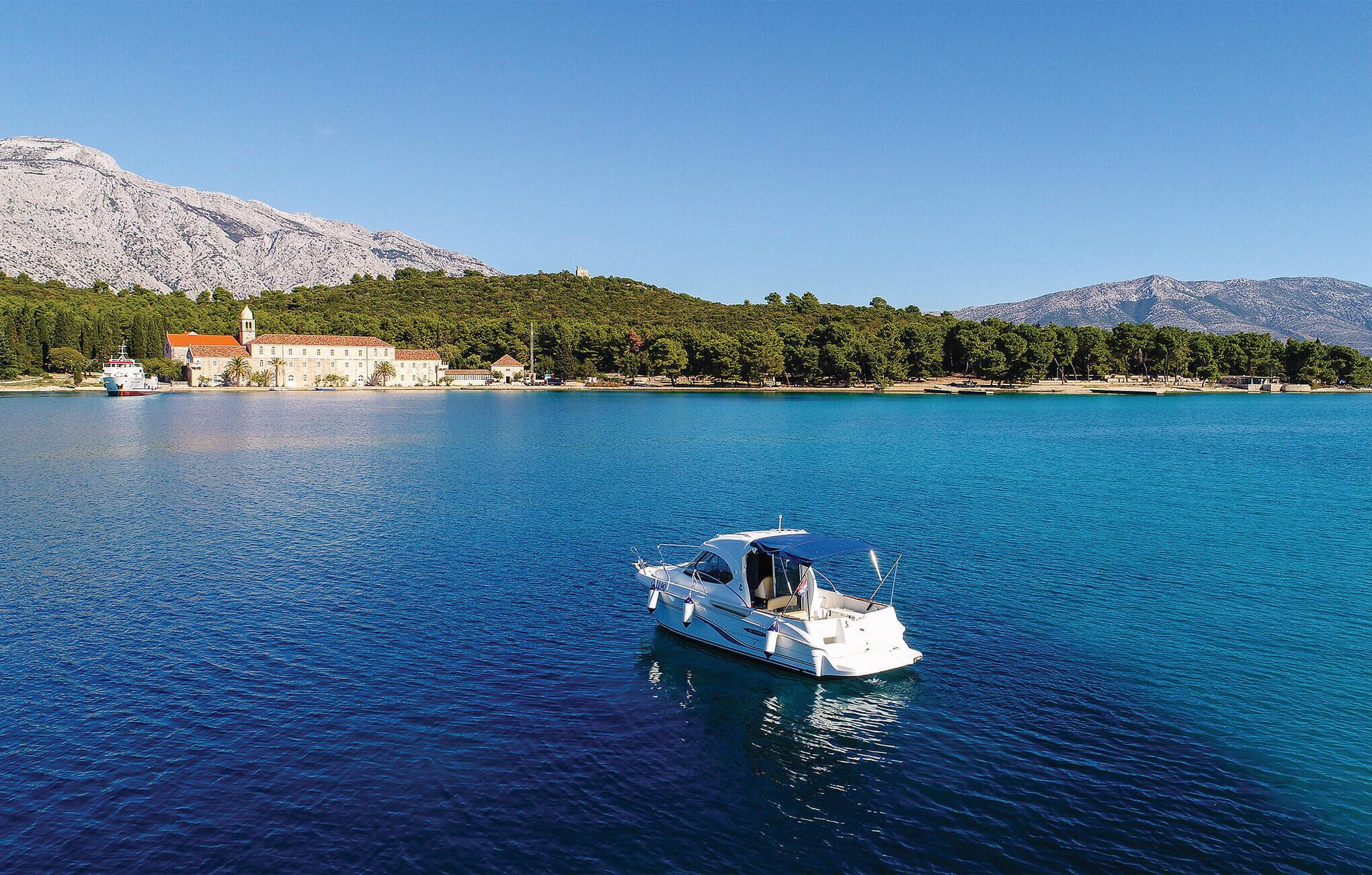 A boat on a calm sea with a coastal building in the background.