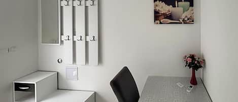 A room with a desk, chair, a mirror, and a framed picture on the wall.