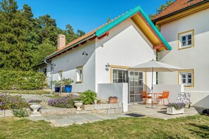 A house with a sloped roof, a patio with outdoor furniture, and a garden with various plants and flowers.