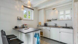 Eine moderne Küche mit weißen Schränken, einer Marmorarbeitsplatte, einem eingebauten Geschirrspüler und einem Fenster mit Jalousien.
