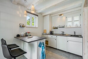 A modern kitchen with white cabinetry, a marble countertop, a built-in dishwasher, and a window with blinds.