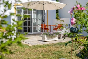 An outdoor patio area with a table and chairs, a large umbrella, and a planter with flowers.