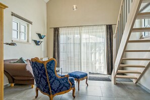 Ein geräumiges Wohnzimmer mit einem blau gemusterten Sessel, einem braunen Sofa, einer Holztreppe und einer großen Schiebeglastür, die zu einem Außenbereich führt.