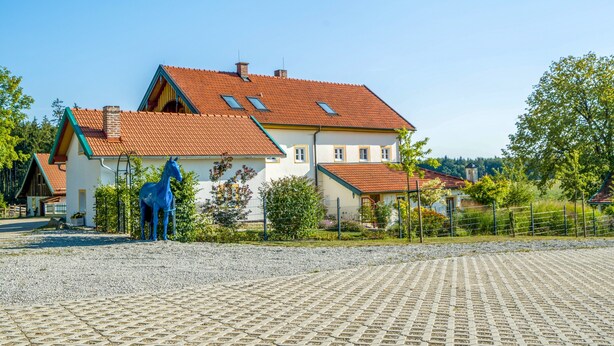 Ein großes Haus mit rotem Ziegeldach, einer Pferdestatue und einem gepflasterten Auffahrt.