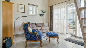 Ein Wohnzimmer mit einer Couch, einem Sessel, einem Couchtisch, einem Bücherregal und einem Fenster mit Vorhängen.
