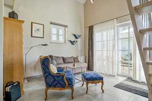 A living room with a sofa, a chair, a coffee table, a bookshelf, and a window with curtains.