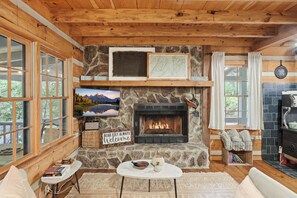 A cozy cabin interior with a stone fireplace, wooden walls, and large windows. - Peace of Aska w/ Hot Tub (Blue Ridge)