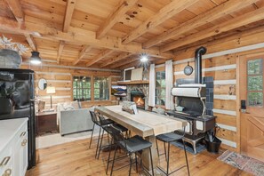 A rustic cabin interior with a stone fireplace, wooden beams, a dining area with chairs, and a television. - Peace of Aska w/ Hot Tub (Blue Ridge)