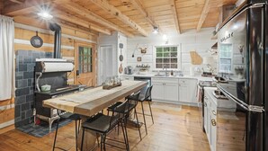 Maalaishenkinen keittiö, jossa on suuri puinen pöytä, musta liesi ja valkoiset kaapit.