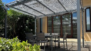 An outdoor patio with a table and chairs, surrounded by greenery and a pergola structure. - A large, charming vacation rental, formerly a wine cellar, located along the Canal du Midi. (marseillette)