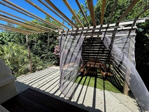 Een pergola van hout met een transparant dak, omringd door grind en begroeiing.