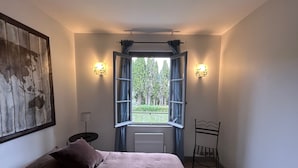 A bedroom with a bed, a nightstand, a chair, a window with curtains, and wall-mounted lights. - A large, charming vacation rental, formerly a wine cellar, located along the Canal du Midi. (marseillette)