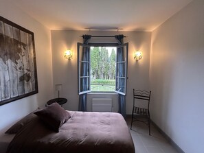 Ein Schlafzimmer mit einem Bett, einem Nachttisch, einem Sessel, einem Fenster mit Vorhängen und Wandleuchten.