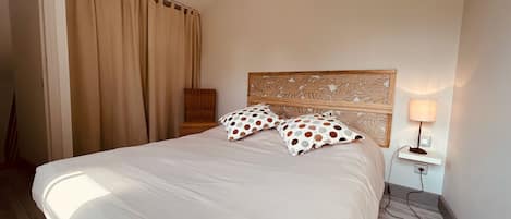 Habitación de hotel con una cama grande, cabecera de madera, mesita de noche con lámpara y una silla.