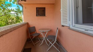 Varanda com uma mesa pequena e duas cadeiras, uma janela com persianas e uma porta.