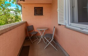A balcony with a small table and two chairs, a window with blinds, and a door. - Gorgeous apartment in Zukve (Zukve)