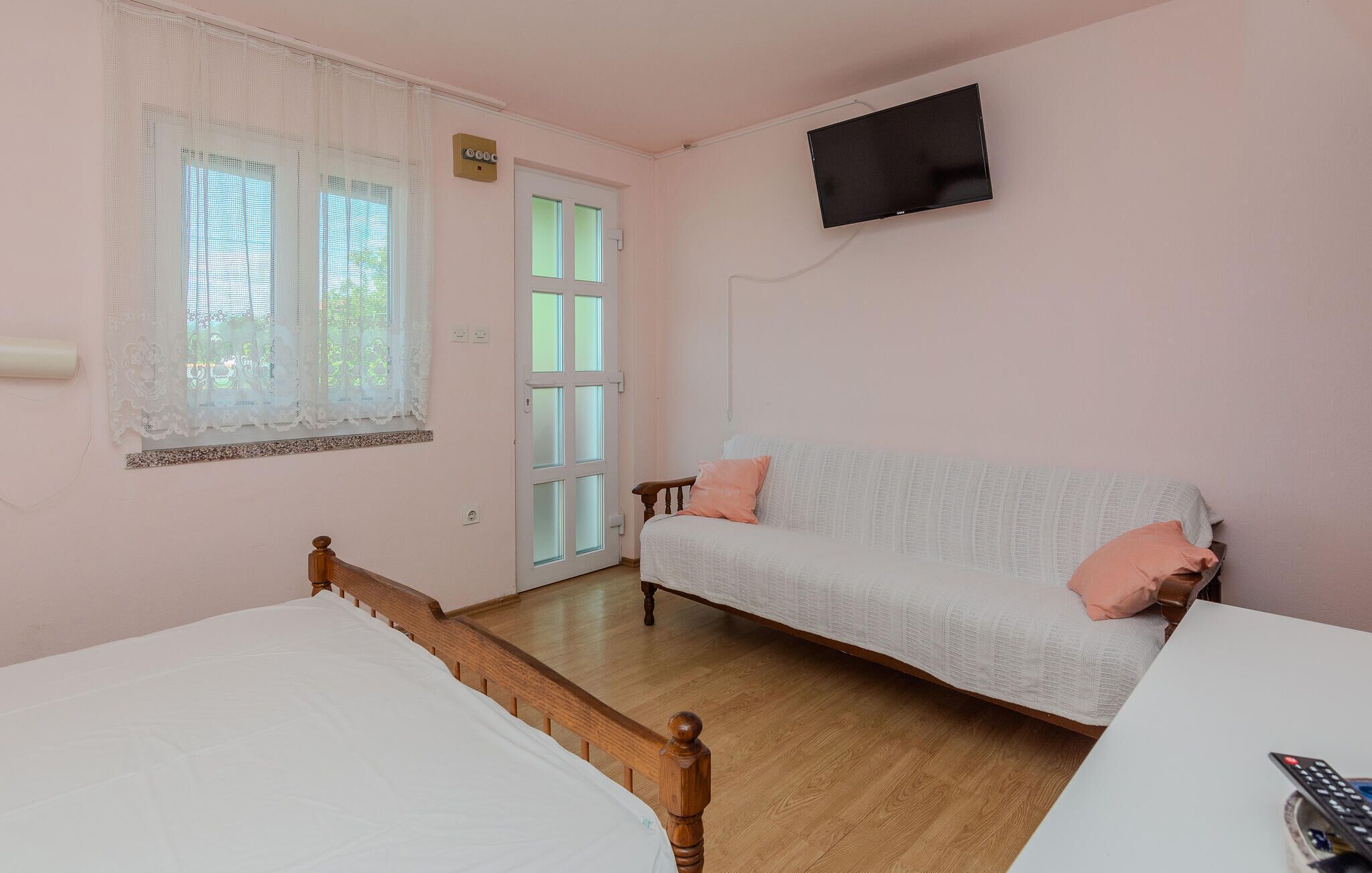 Ein Schlafzimmer mit zwei Betten, einem Schlafsofa, einem Fernseher und einem Fenster mit Spitzenvorhängen.
