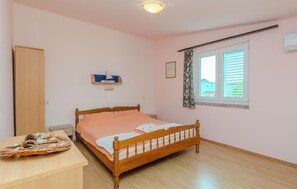 Ein Schlafzimmer mit einem hölzernen Bett, einem Nachttisch mit einer Dekoration, einem Fenster mit Jalousien und einer Tür.