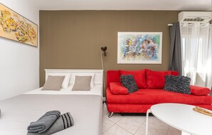 A hotel room with a bed, a red sofa, a white table, and two paintings on the wall. - Beautiful apartment in Biograd na Moru with WiFi (Biograd na Moru)