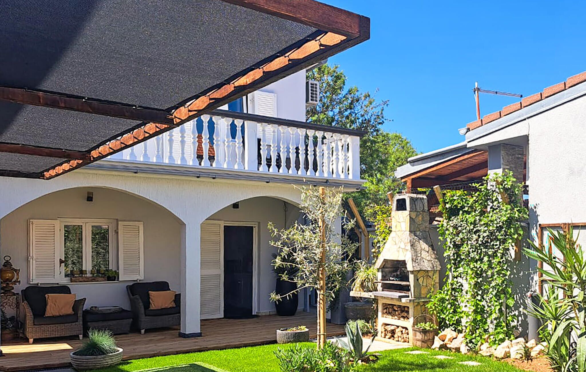Una propietat residencial amb terrassa coberta, zona d'seients exteriors i una barbacoa de pedra.