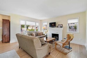 Ein Wohnzimmer mit Sofa, Sessel, Kamin und Fernseher.