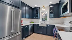A modern kitchen with dark cabinetry, stainless steel appliances, and a central island. - Classic 3 Bedroom Eastport Cottage with Large Yard and Free Parking (Annapolis)